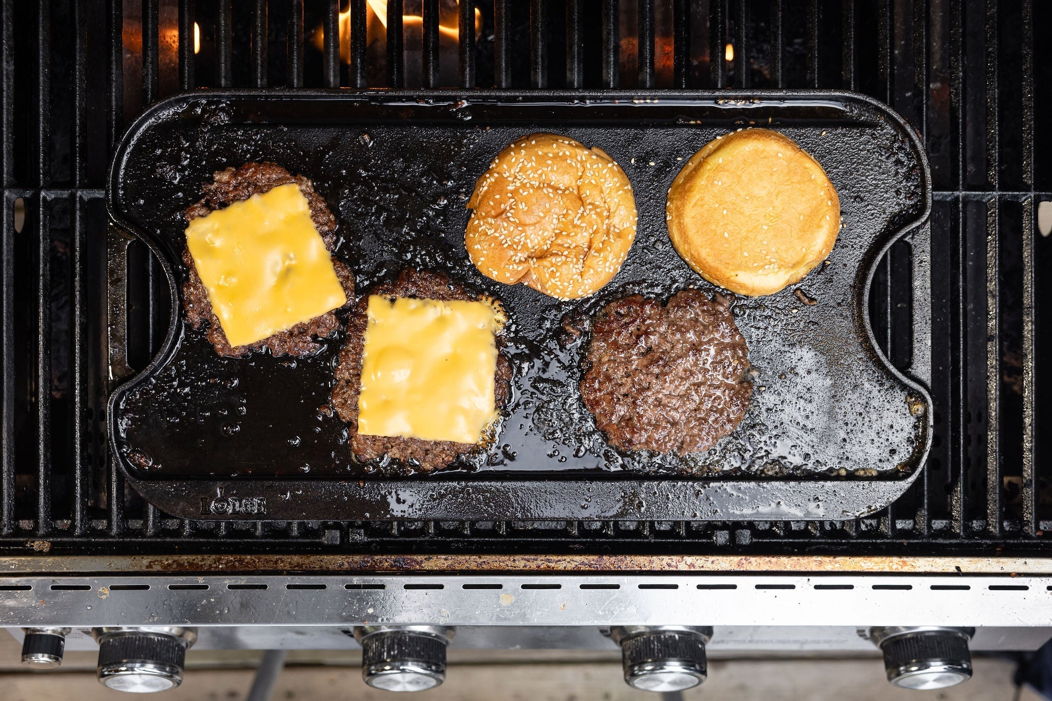 Smash burgers cooking on griddle with cheese and buns.