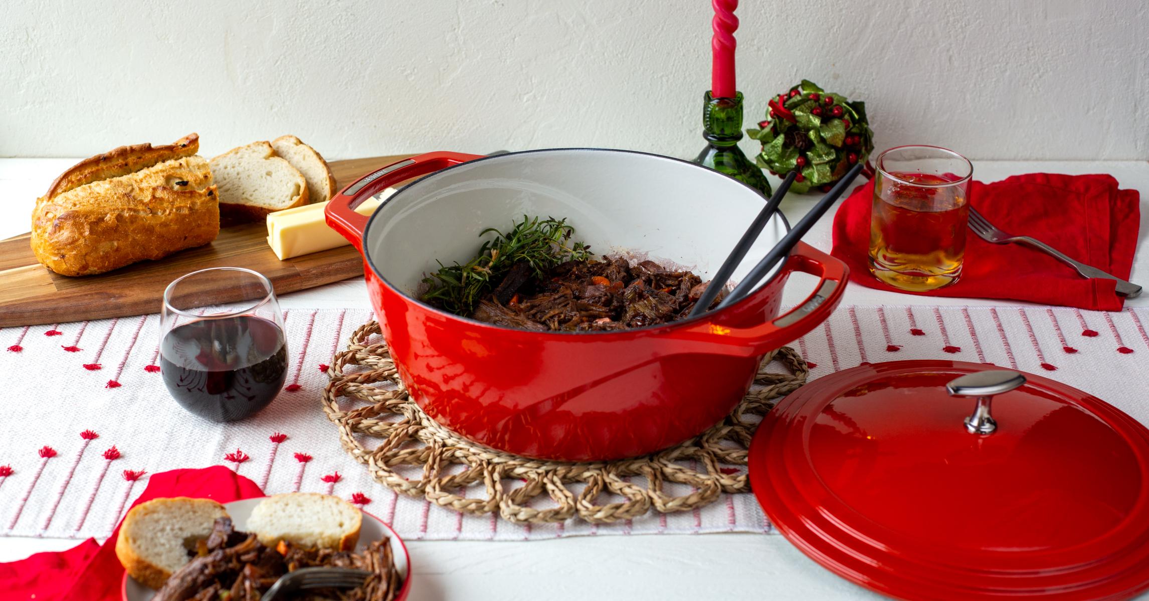 Pot roast served from red dutch oven with bread and red wine.