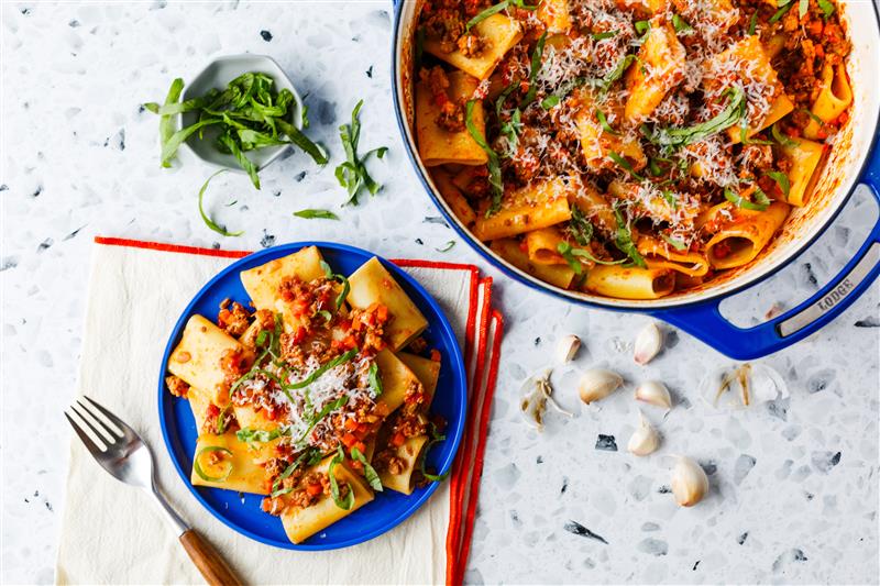 Pasta Bolognese served on table near dutch oven full of freshly prepared pasta.