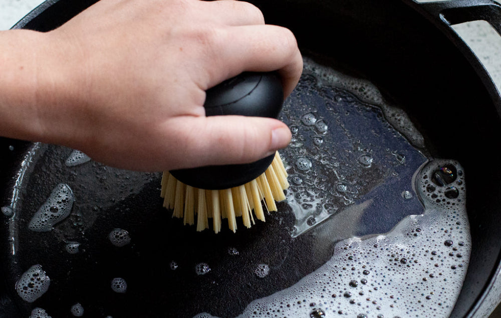 Someone scrubbing a skillet with soapy water