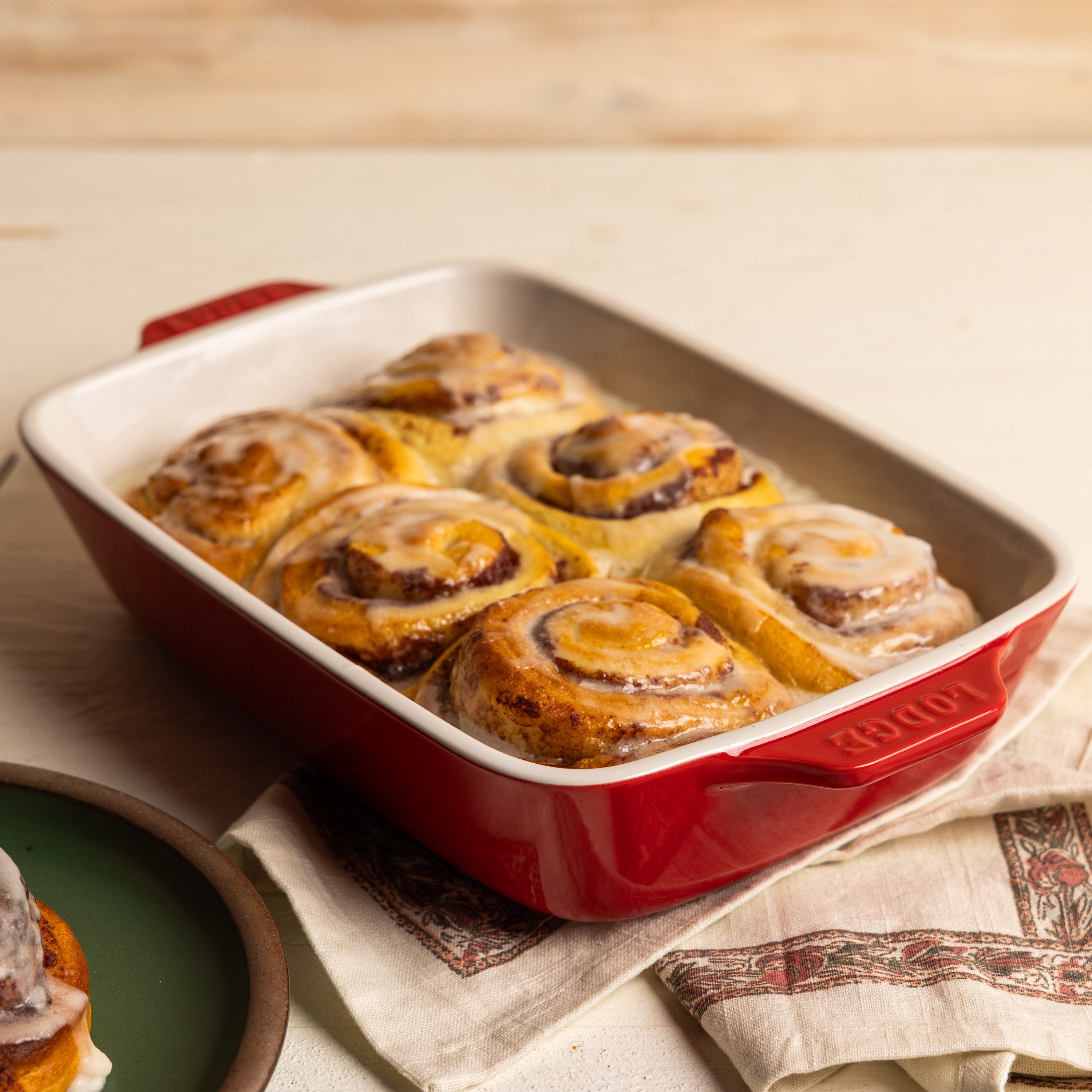Baked cinnamon rolls in a red ceramic dish.