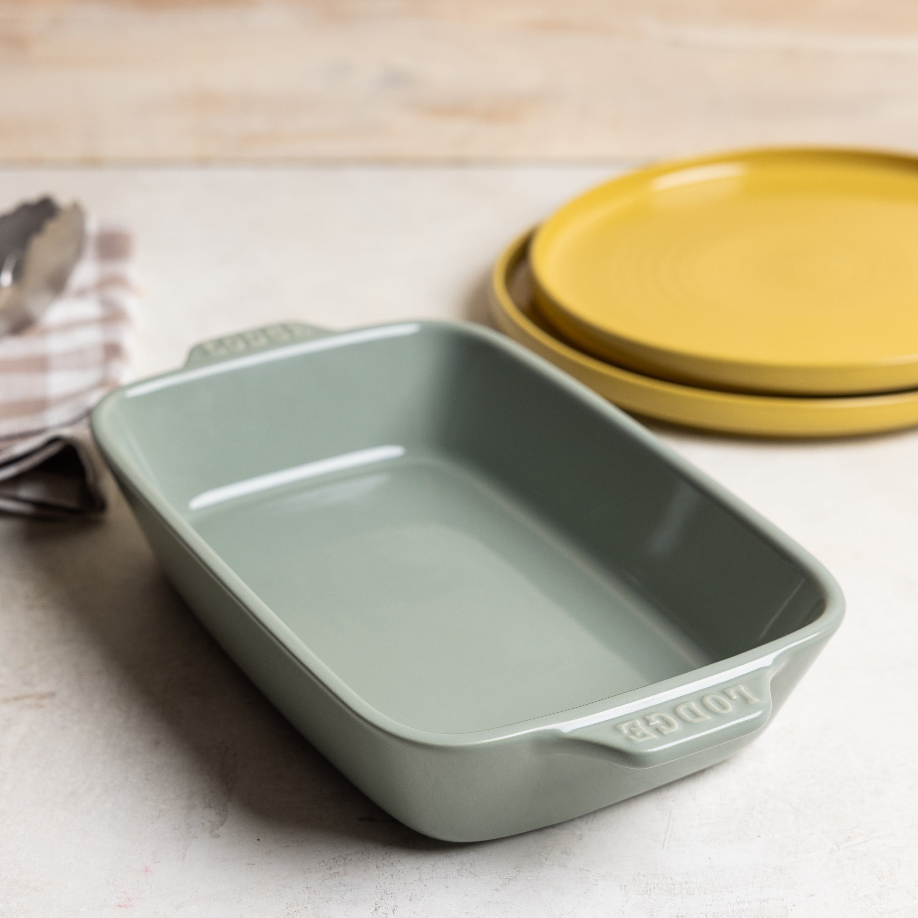 Desert-sage ceramic casserole dish near yellow plates.