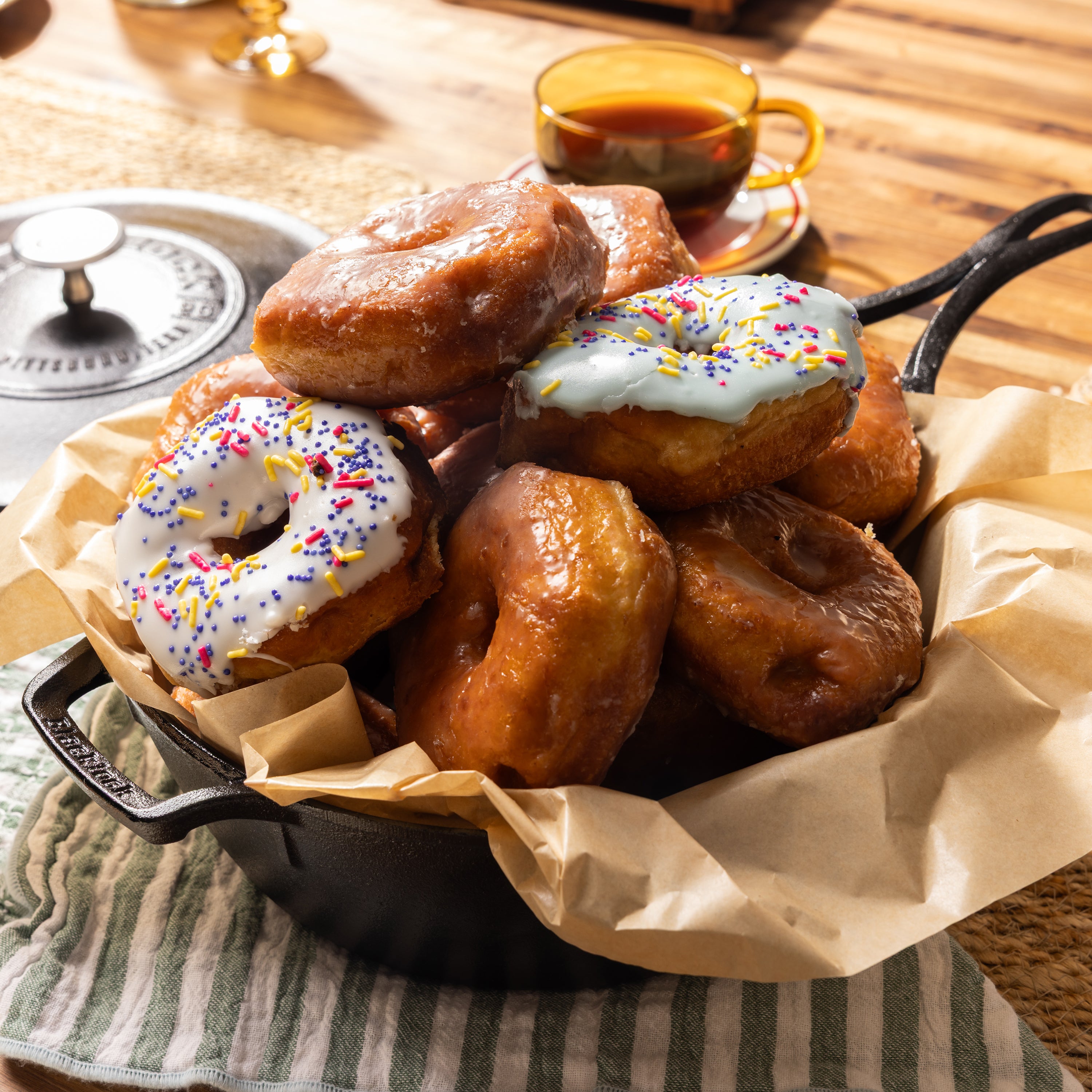 Freshly made donuts in dutch oven, someone are glazed and some are frosted with sprinkles.