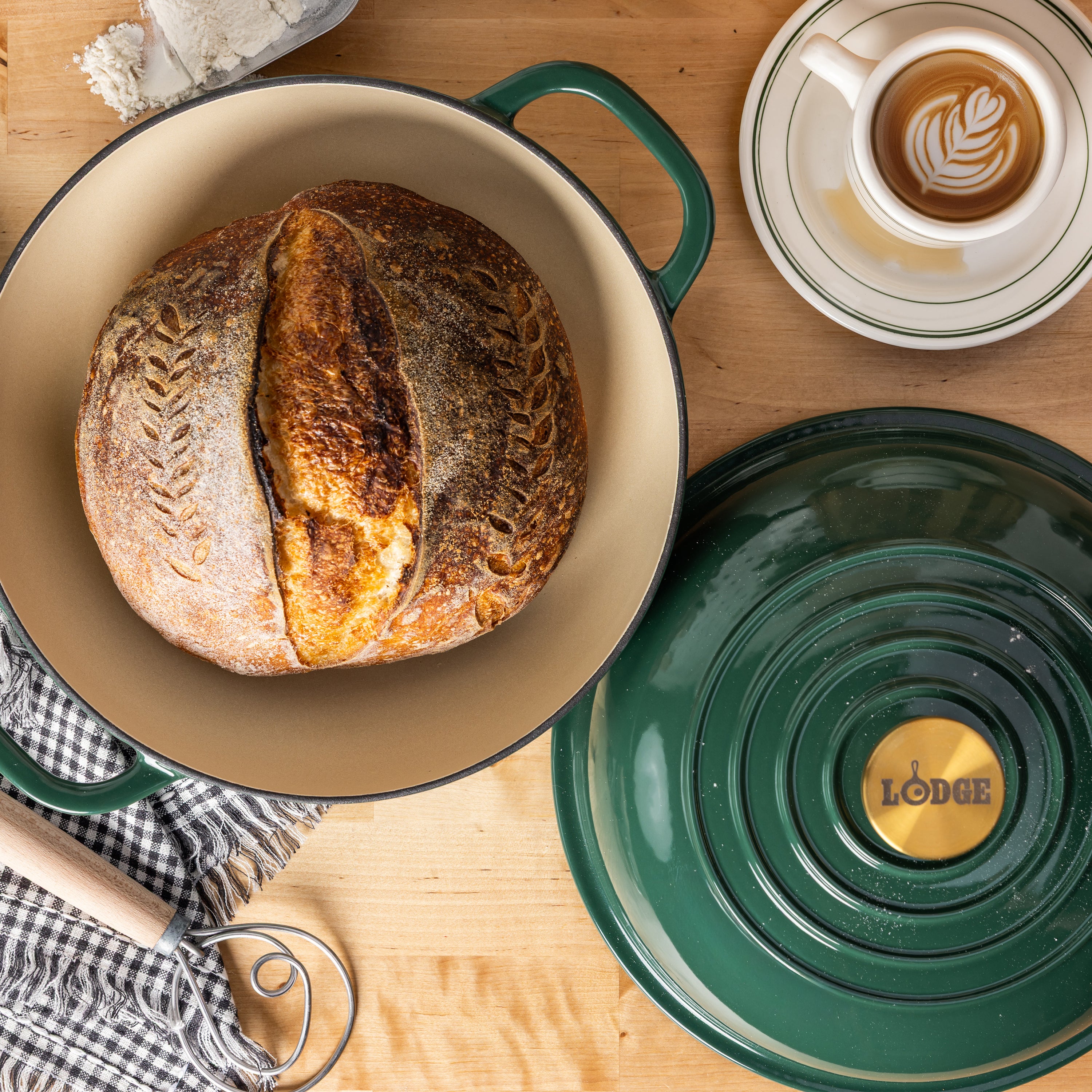 A Lodge enameled cast iron round bread oven with its lid off, showing a rustic artisan sourdough bread inside and a tan interior.