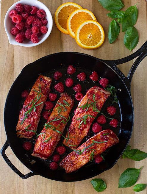 Our pan seared salmon recipe with raspberry basil sauce, served in skillet alongside fresh ingredients.