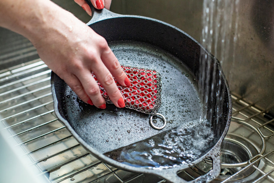 Someone scrubbing skillet with chainmail scrubber under running water.