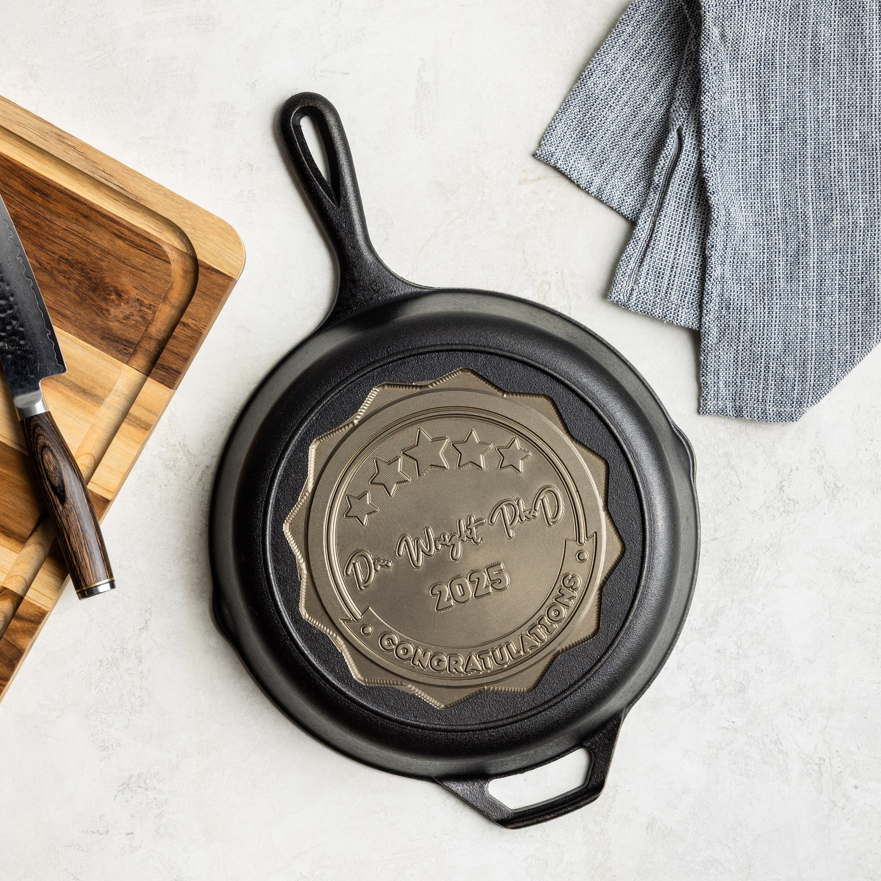 Black cast iron skillet with engraved design on a light surface with a wooden cutting board and knife.