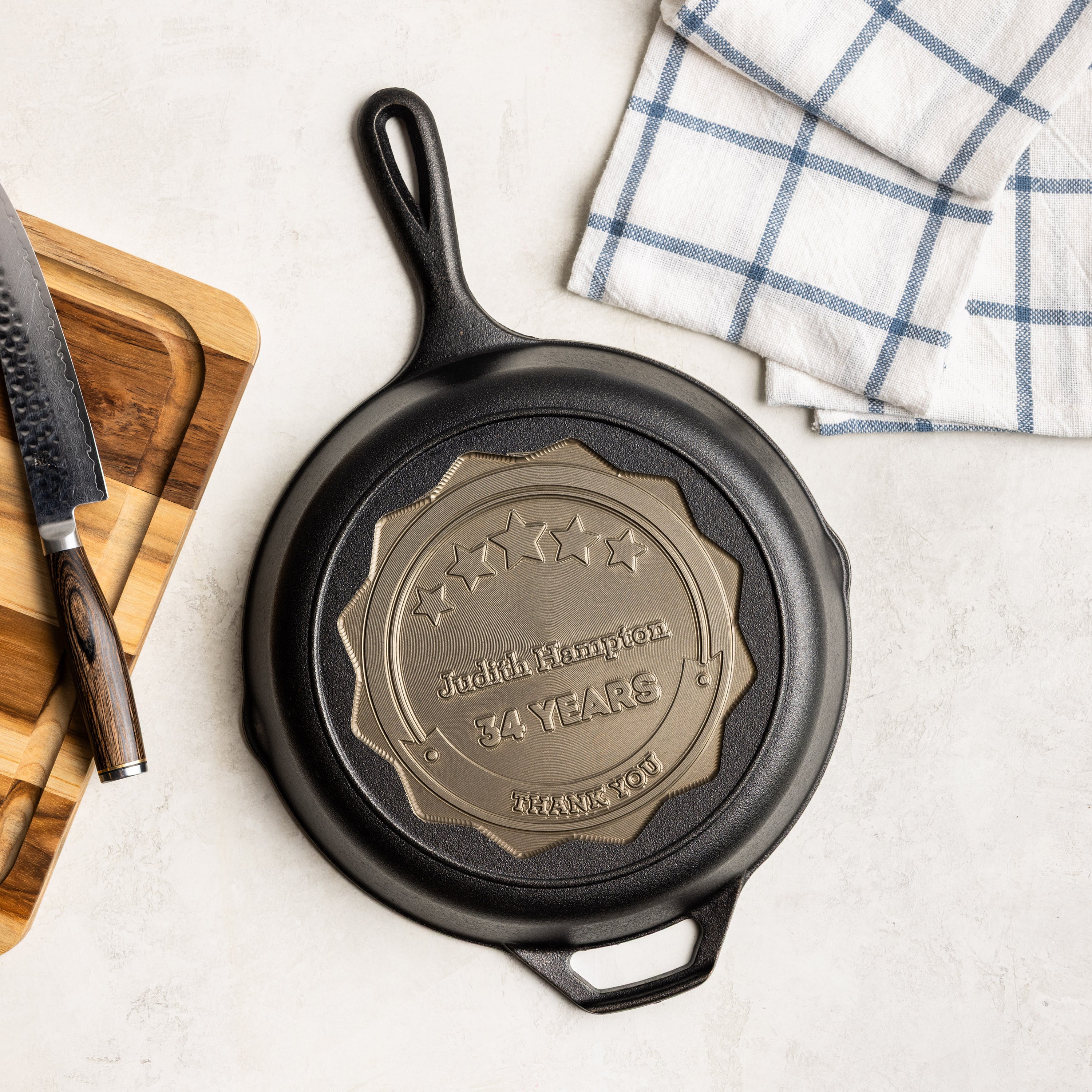Black cast iron skillet with engraved message on a light surface with a cutting board and towel.