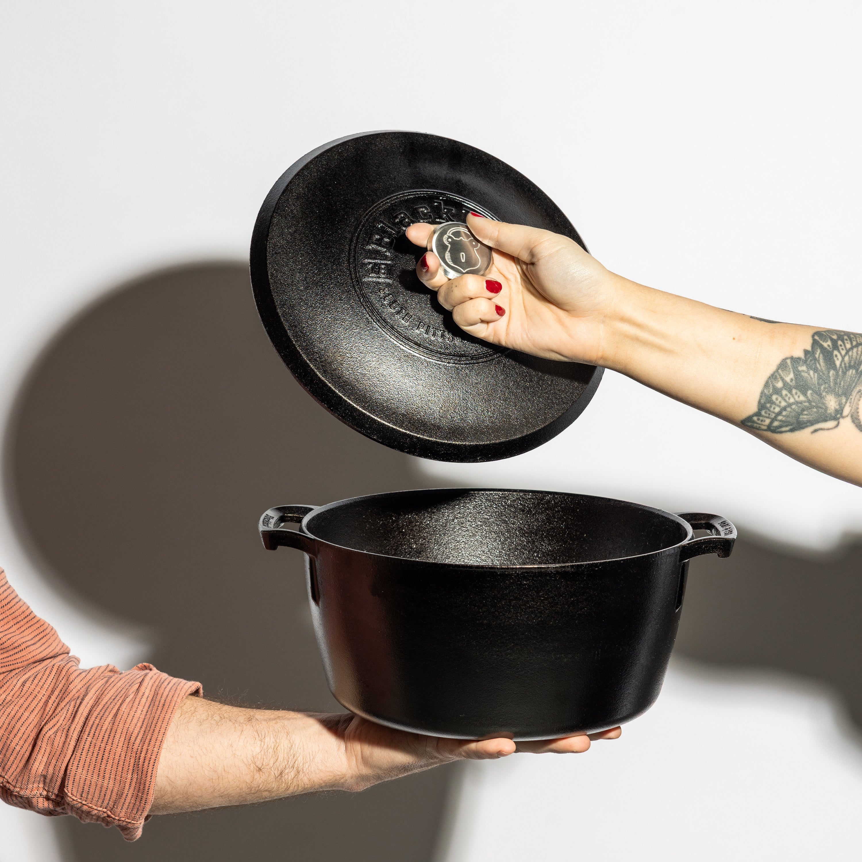 Someone holding dutch oven while someone else lift's the lid.