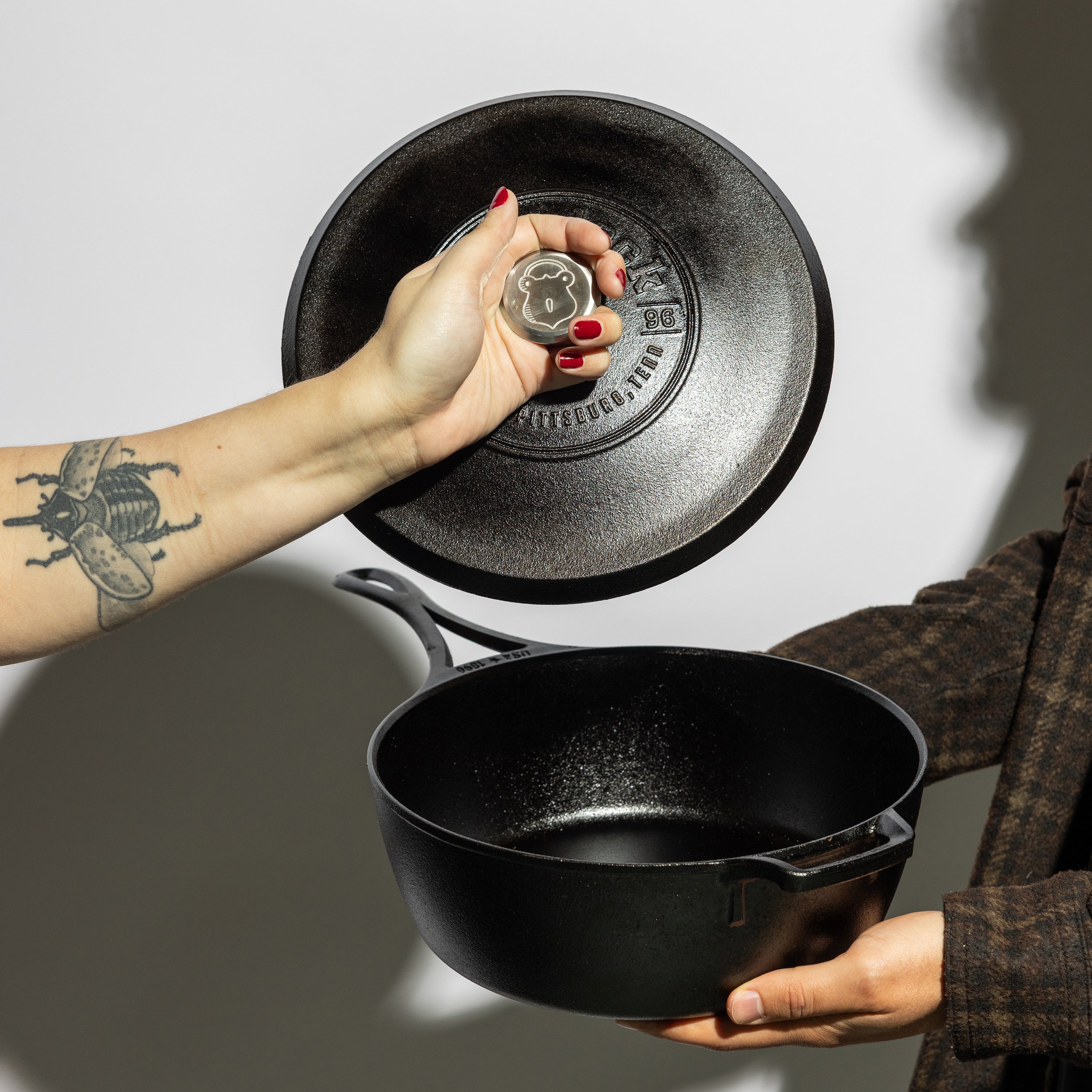 Someone holds skillet displaying cooking area and someone else holds lid by silver knob.
