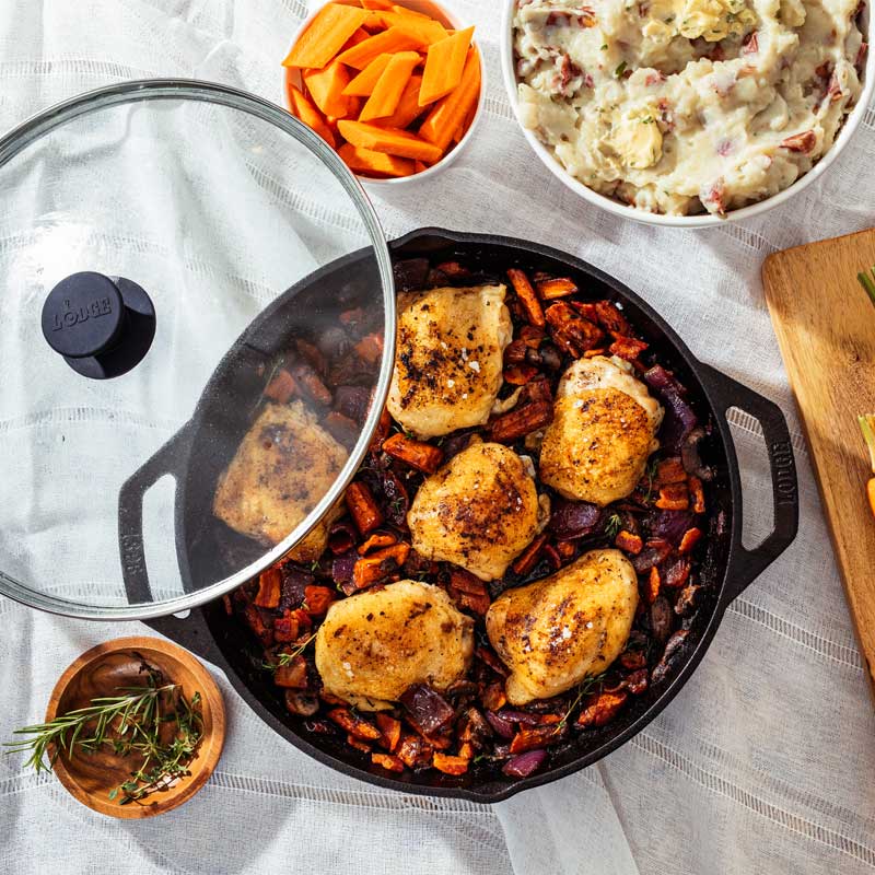 Chicken dish presented on table with pan alongside mashed potatoes and carrots.