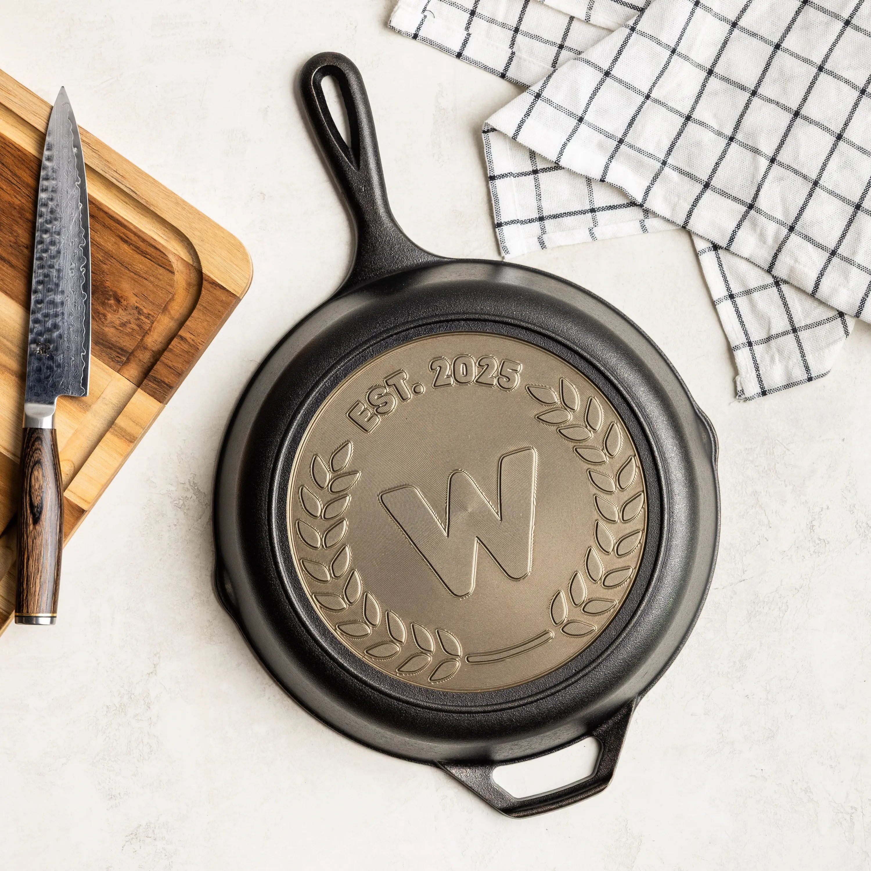 Black cast iron skillet with engraved design on a white surface with a knife and cutting board.
