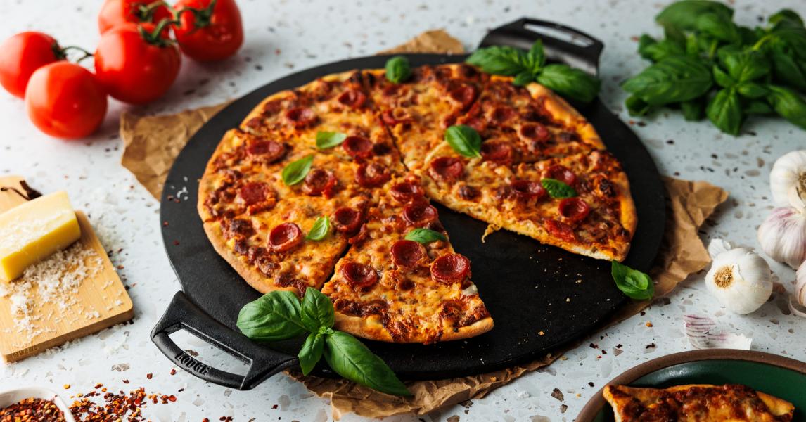 Thin crust pizza, topped with pepperoni and basil, served from pizza pan on table.