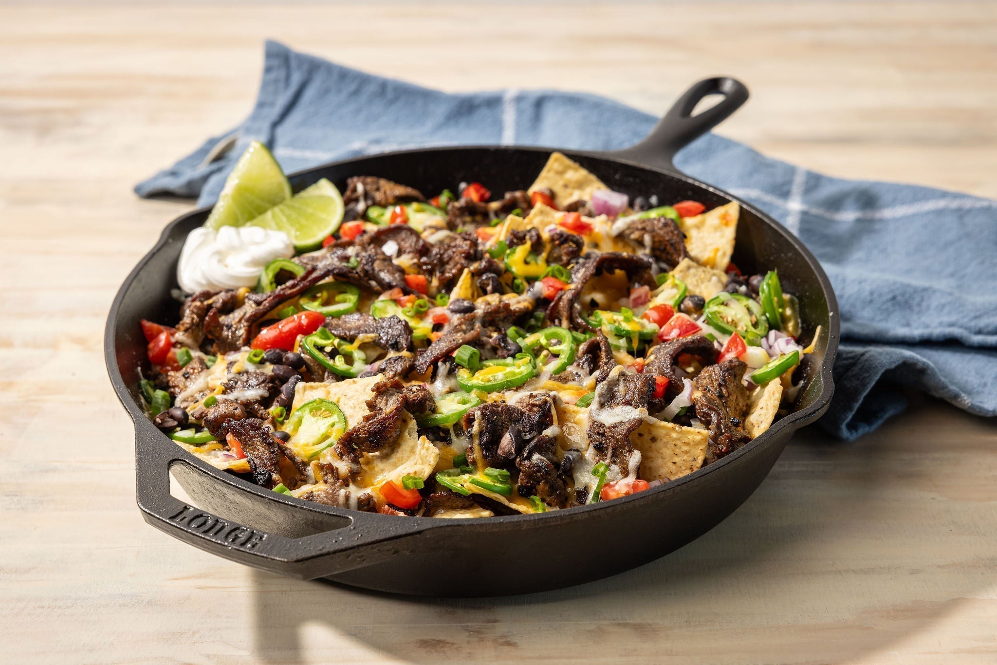 Steak nachos serve from skillet with limes.