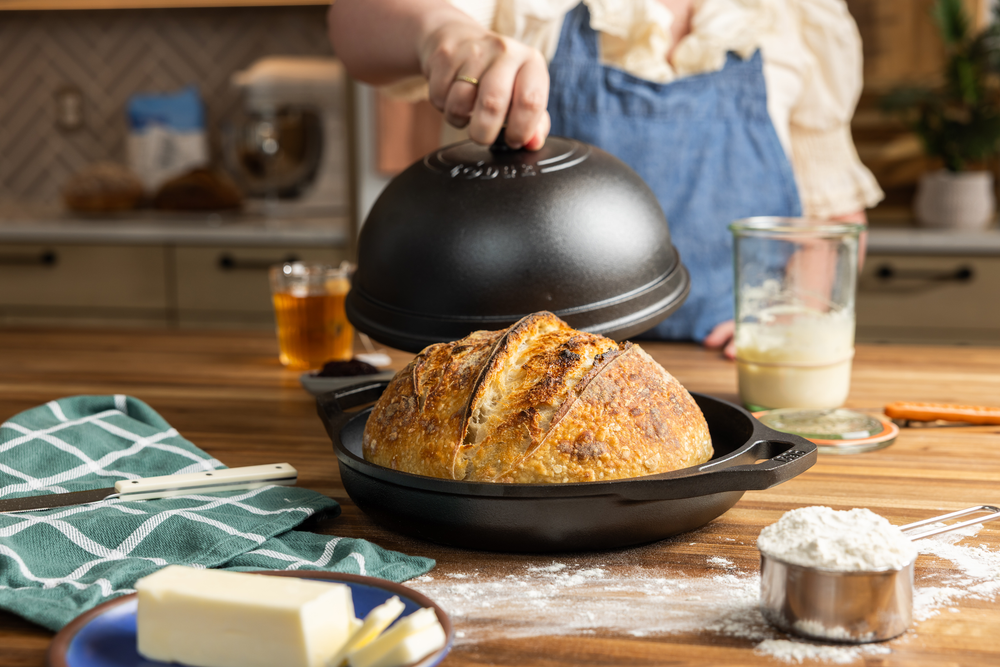 Someone lifting lid off of bread oven revealing a sourdough loaf