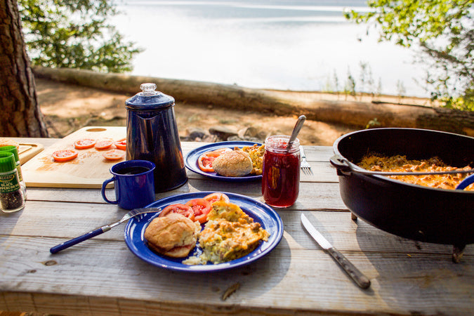 Mountain ma breakfast served with blue plates on picnic table near lake
