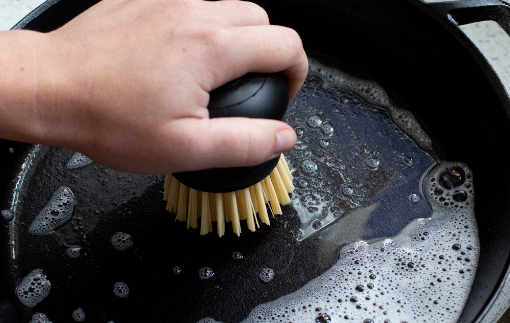 Someone scrubbing a skillet with soapy water