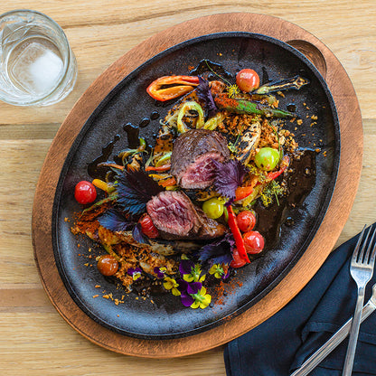Steak and veggie meal served on griddle with wood underliner.