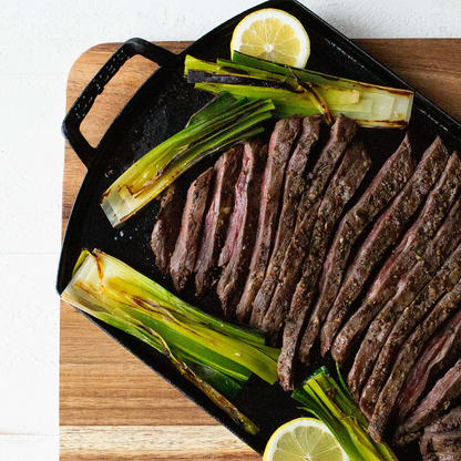 Sliced steak with lemons and green onions on griddle over a wooden board.