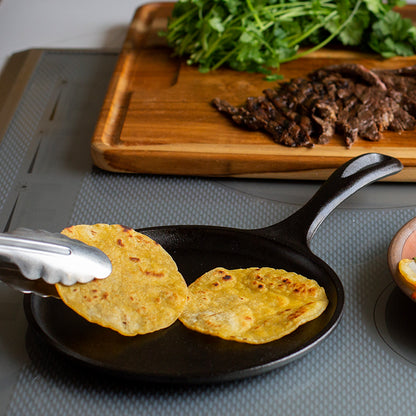 Someone flipping cooked tortillas on griddle to use for their steak tacos.