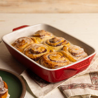 Baked cinnamon rolls in a red ceramic dish.