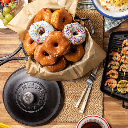 Top view of kitchen table filled with dishes including donuts prepared in skillet.