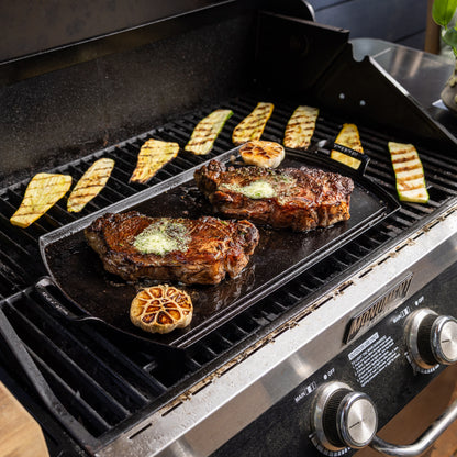 Griddle on a grill cooking steak.