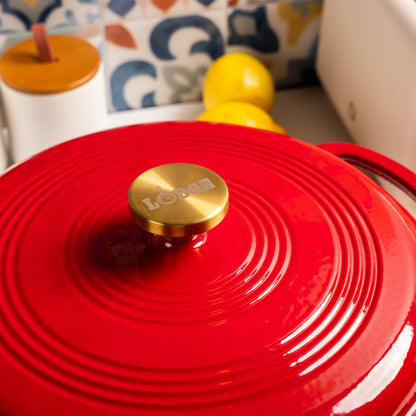 Red lid with a gold knob featuring the brand 'Lodge' on a blurred kitchen background.