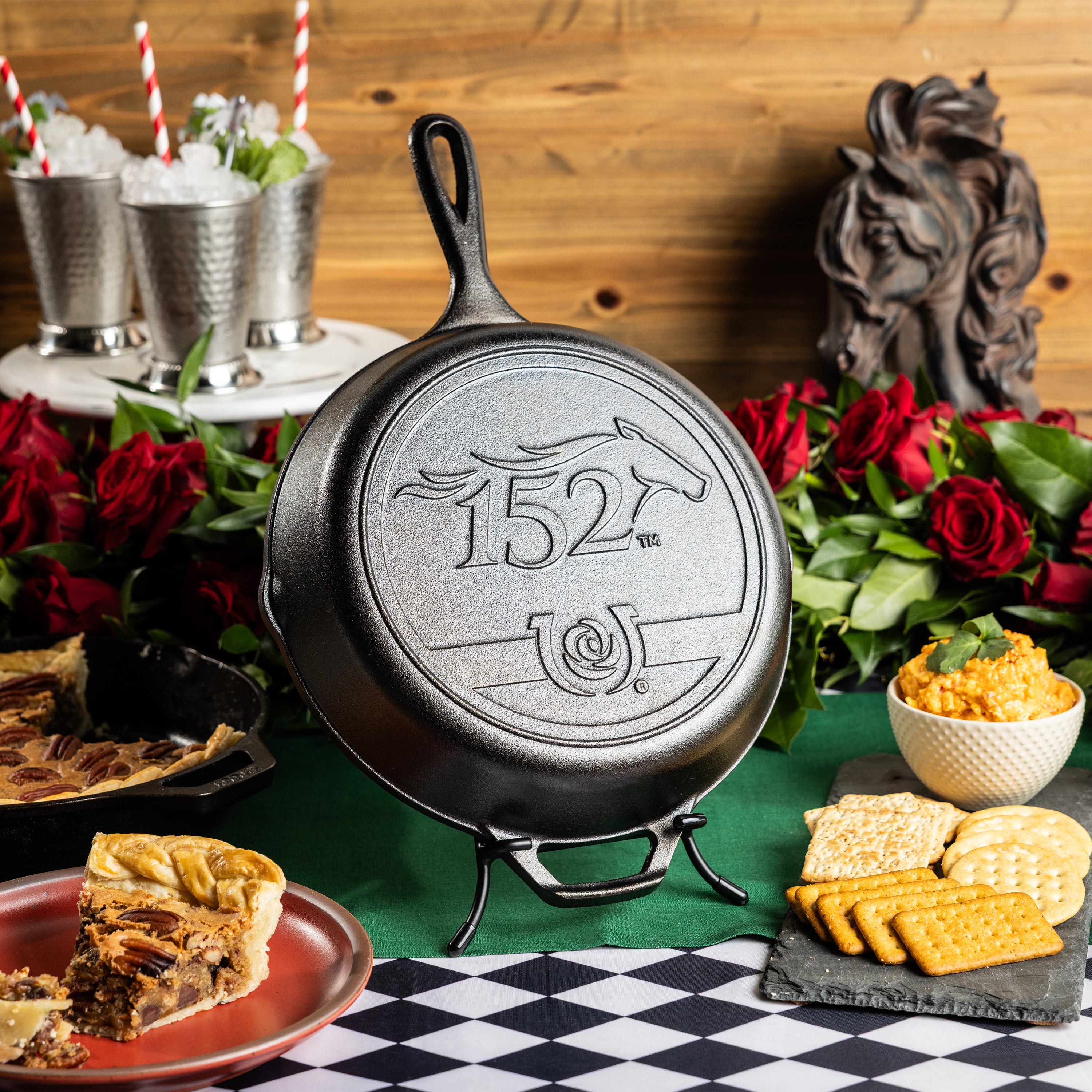 Kentucky Derby skillet, featuring the 152nd year logo, displayed beside mint julep's, roses, and other food.
