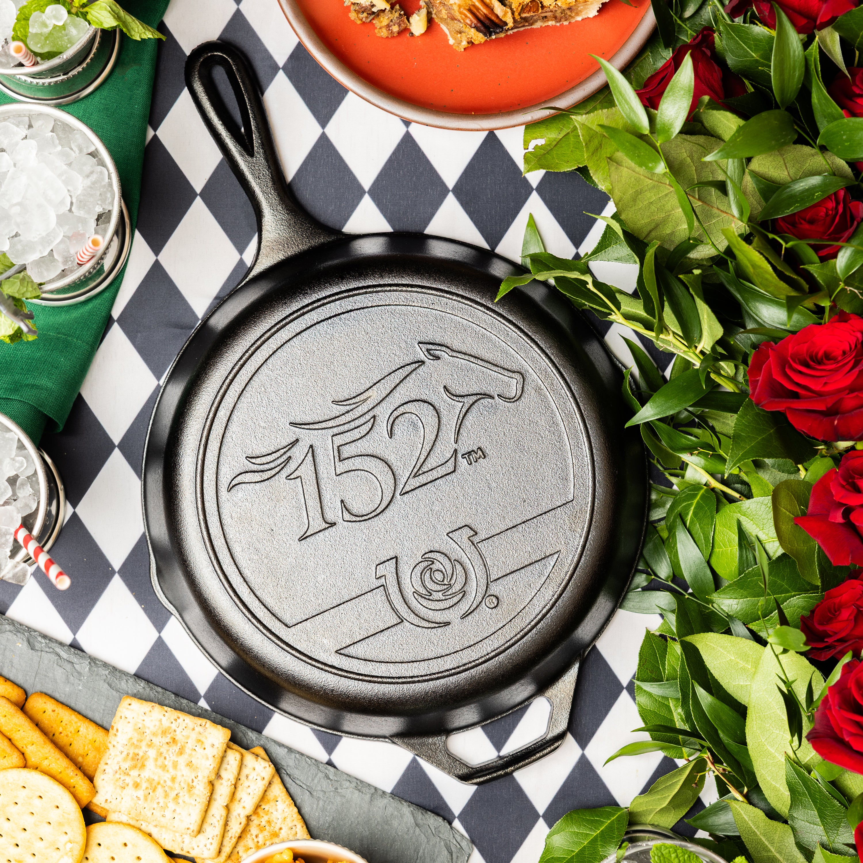 Seasoned Cast Iron Kentucky Derby Skillet for the 152nd year, placed on checkered table surrounded by food and roses.