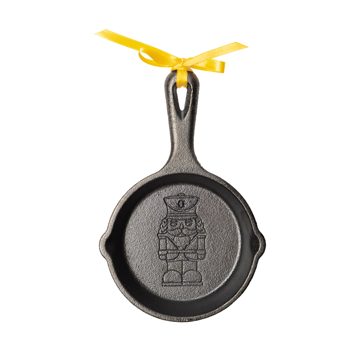 A decorative cast iron skillet ornament featuring an embossed nutcracker design in the center, suspended by a bright yellow ribbon on a plain white background.
