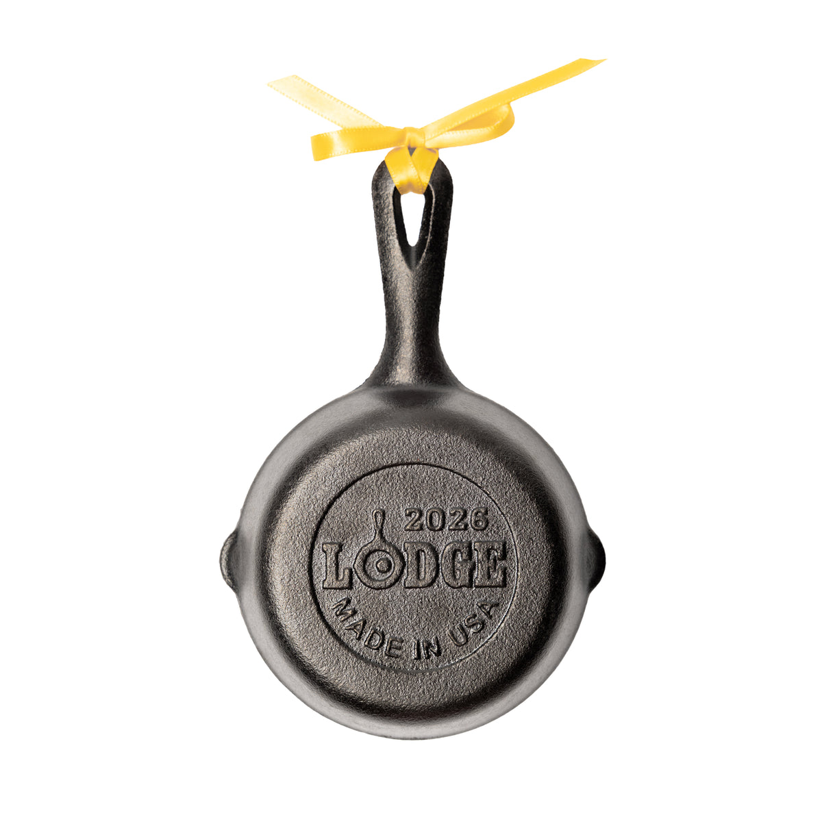 A cast iron skillet-shaped ornament with a yellow ribbon bow, featuring an embossed 'Lodge' logo and '2026 Made in USA' on the back.