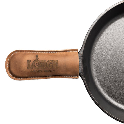 Close-up of a cast iron skillet handle covered with a tan leather sleeve embossed with the Lodge Cast Iron logo, on a white background.
