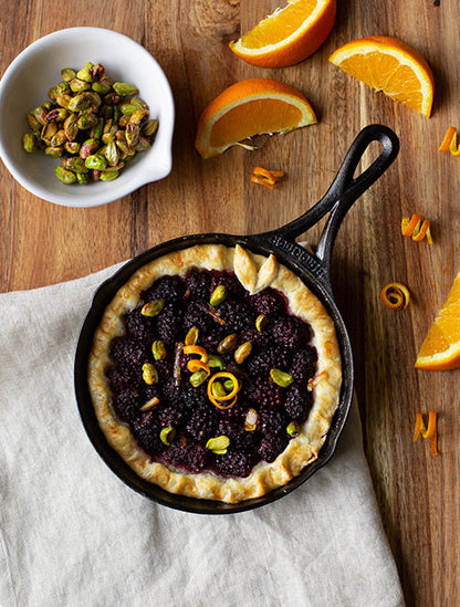 Freshly made blackberry tart with orange garnish served in skillet.