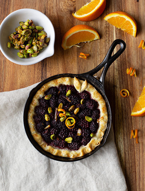 Freshly made blackberry tart with orange garnish served in skillet.