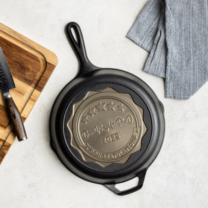 Black cast iron skillet with engraved design on a light surface with a wooden cutting board and knife.