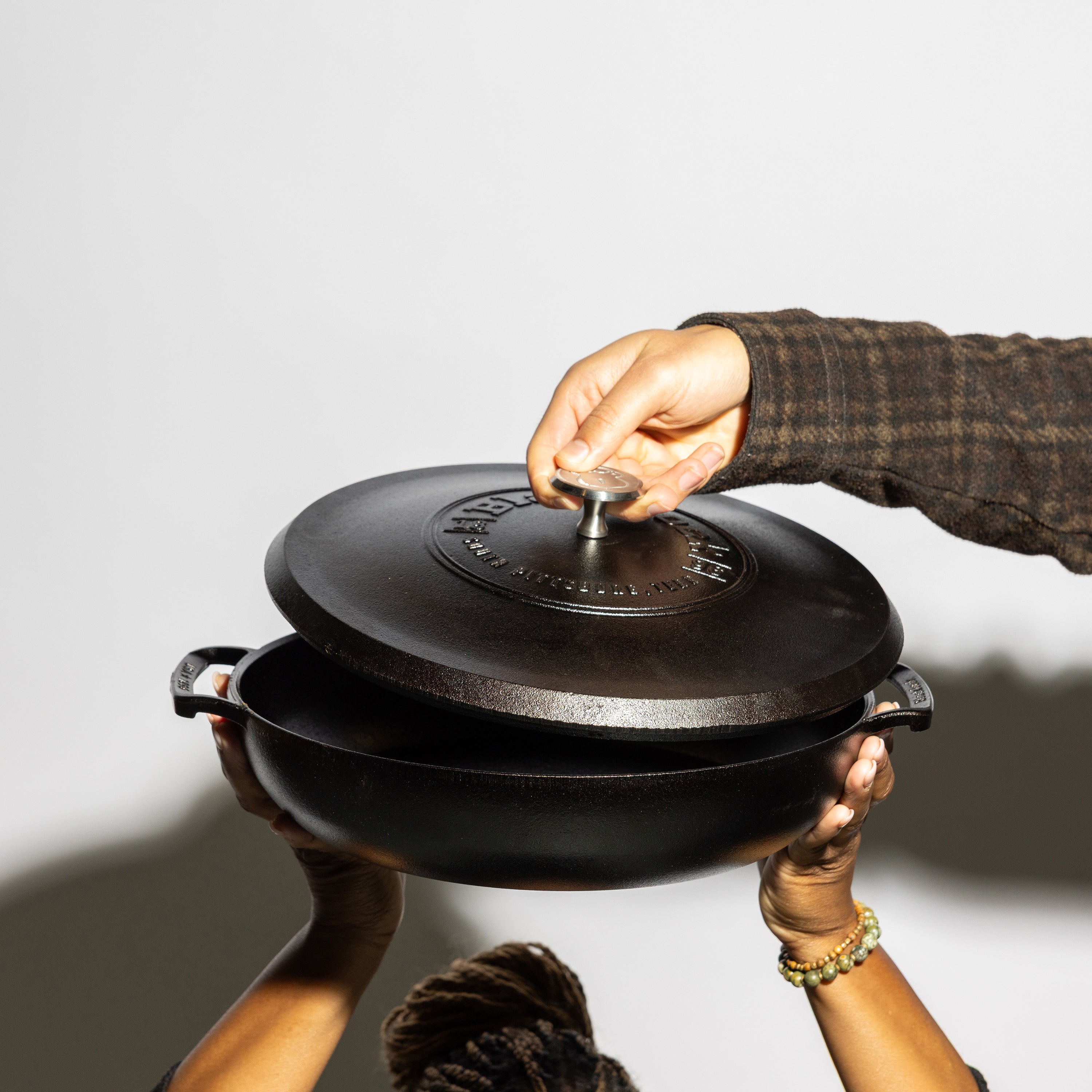 Someone holding braiser while someone lifts lid.