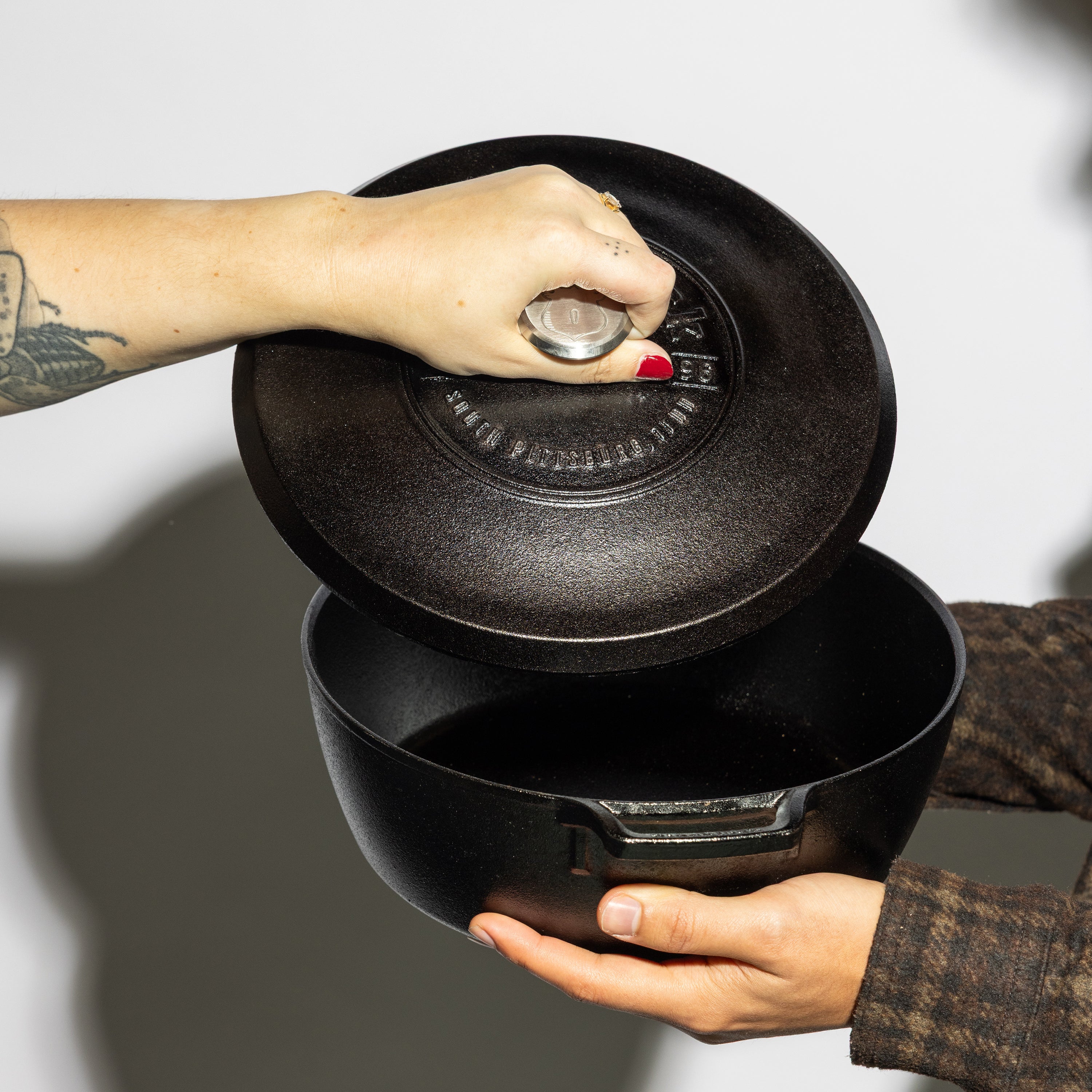 Someone holding skillet while some else removes lid.