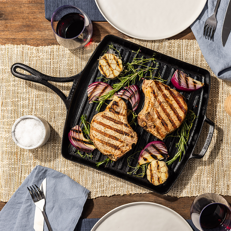 Grilled pork chops with vegetables presented on pan on a dining table.