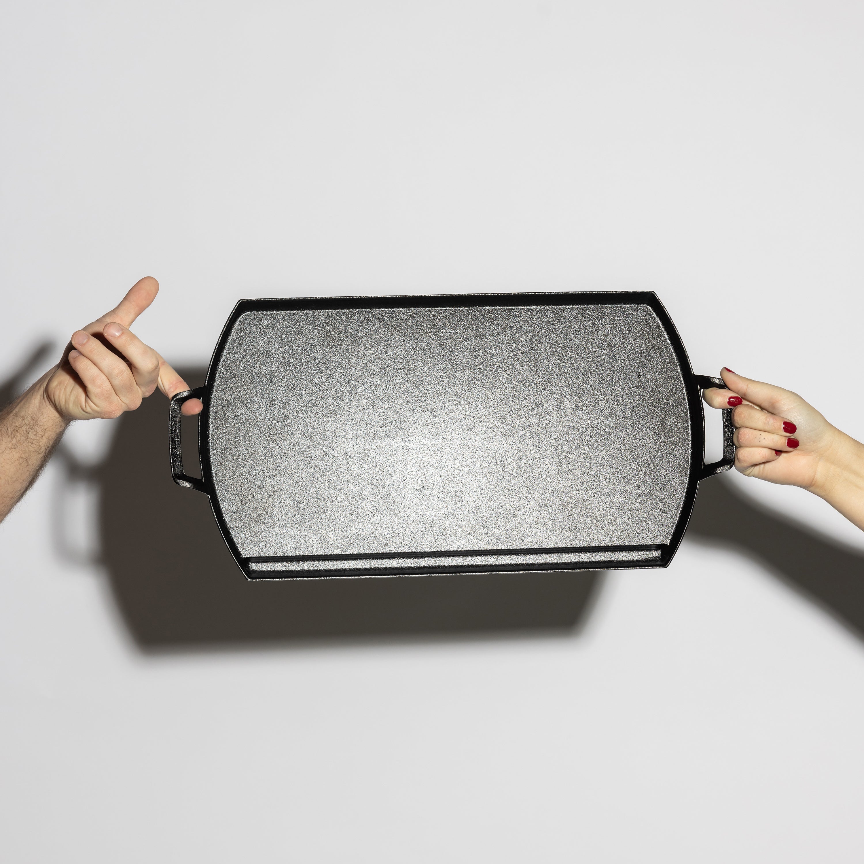 Two people holding griddle showing cooking surface.