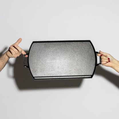 Two people holding griddle showing cooking surface.