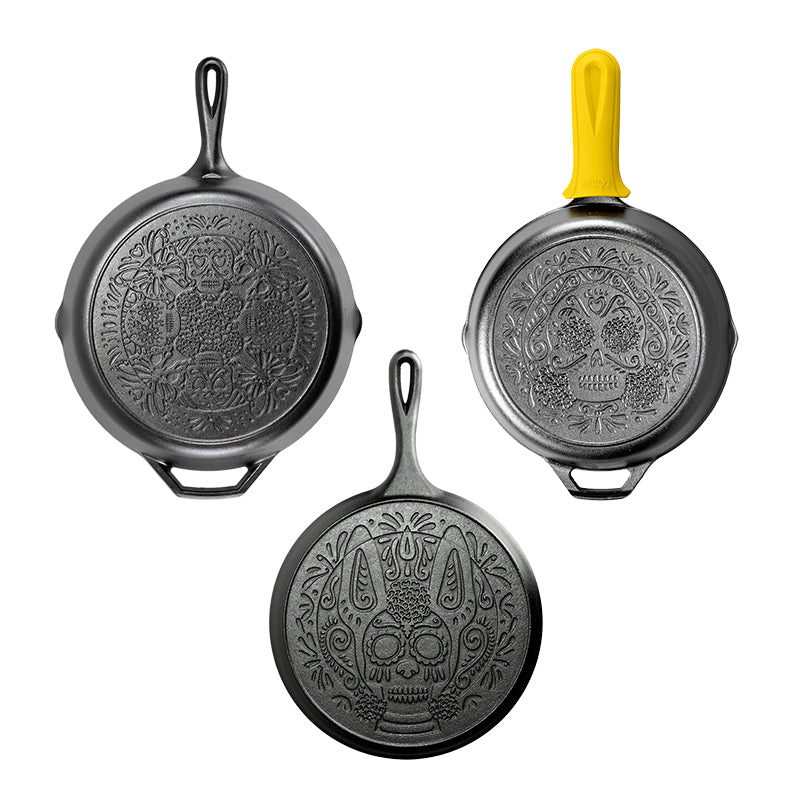 Three cast iron skillets with skull designs including a yellow silicone handle holder.