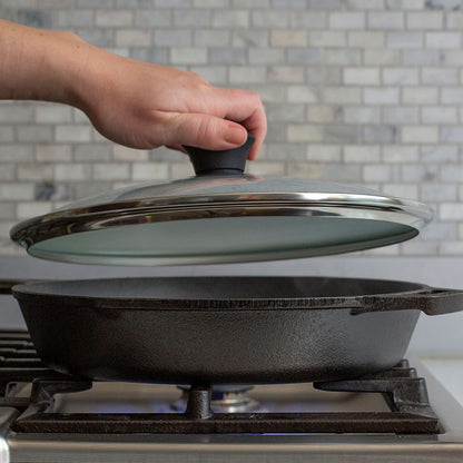 Someone placing lid on skillet while cooking on stove.