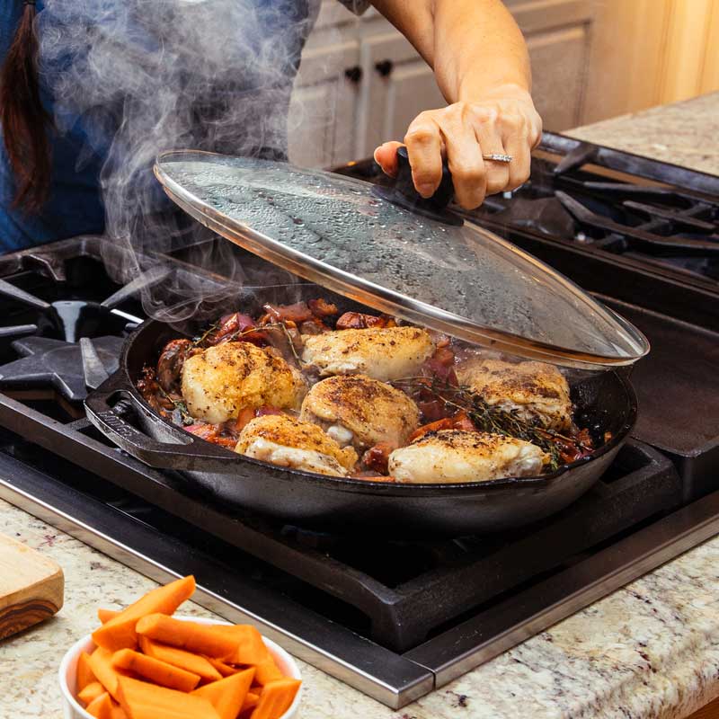 Someone taking lid off of pan while cooking chicken on stove.