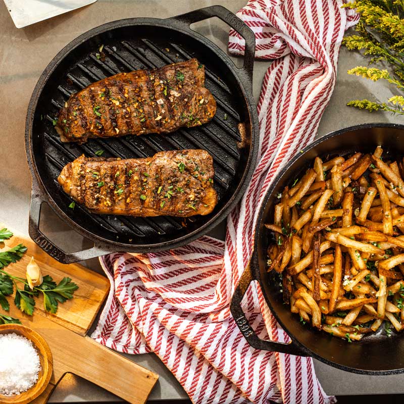 Steak frites cooked using both pieces of dutch oven presented on table.