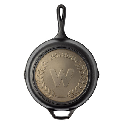 Black cast iron skillet with a gold emblem and 'W' logo on a white background