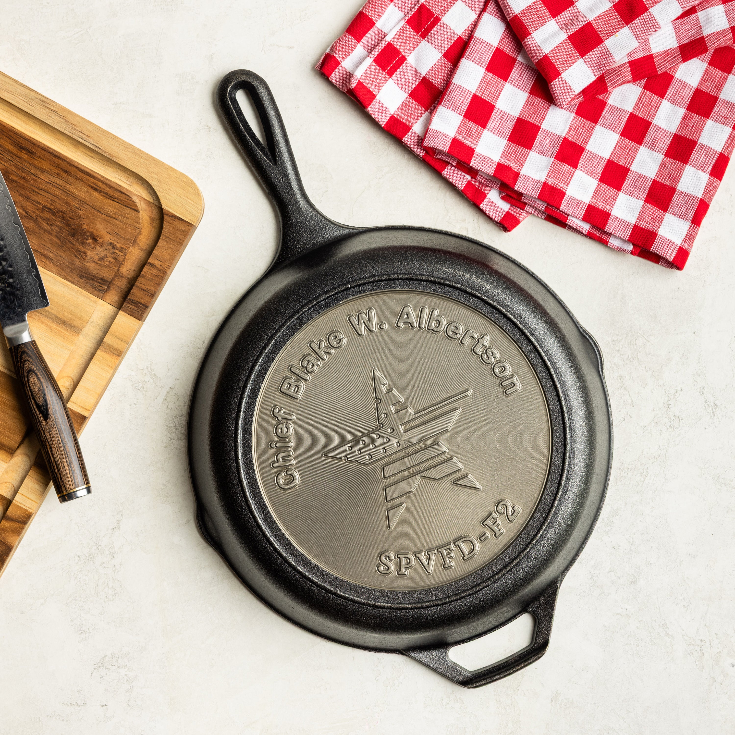 Black cast iron skillet with engraved star design on a white surface with red checkered towels and wooden cutting board.