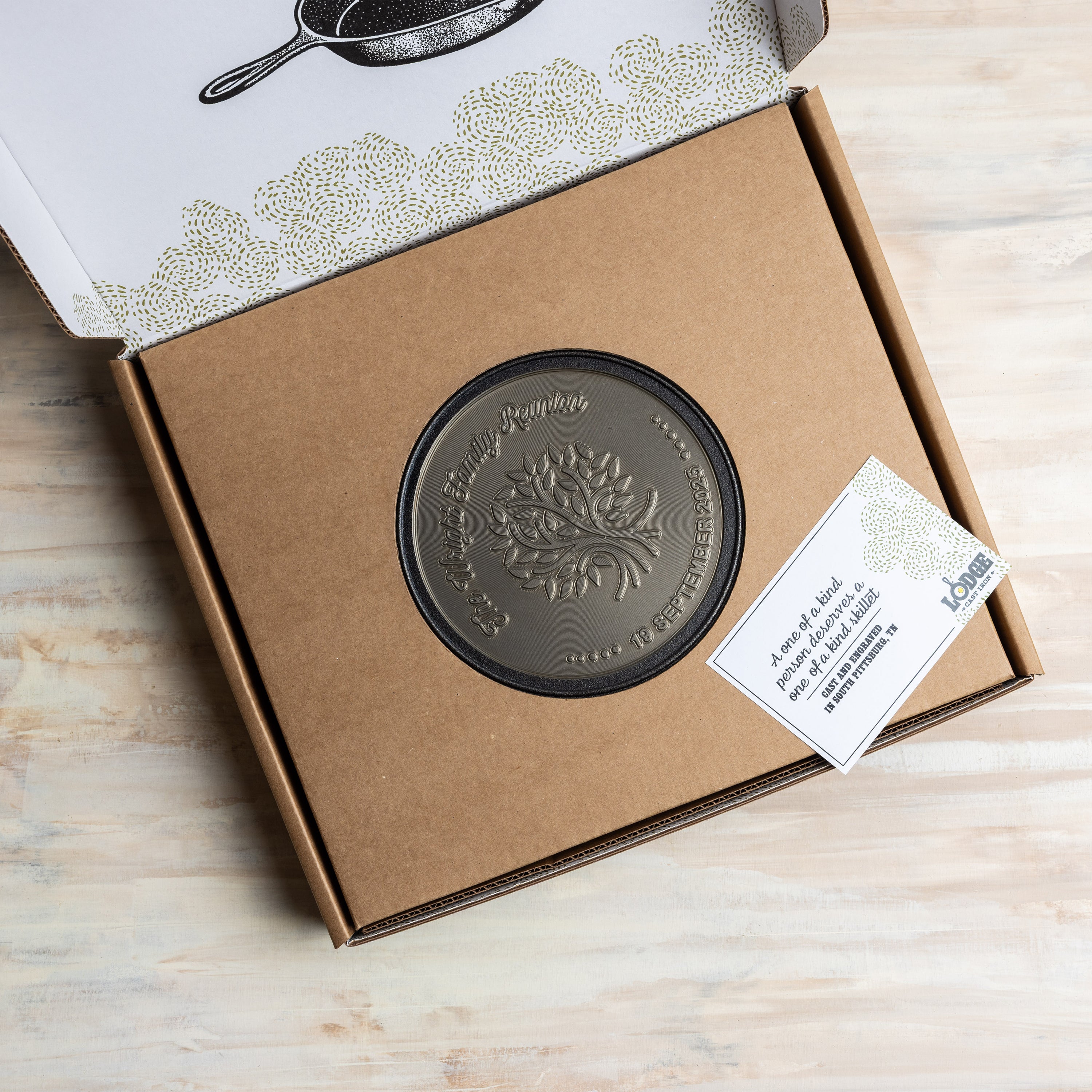 Bronze-colored engraved design in a cardboard box with a tag, on a wooden surface.
