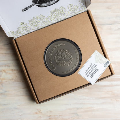 Bronze-colored engraved design in a cardboard box with a tag, on a wooden surface.
