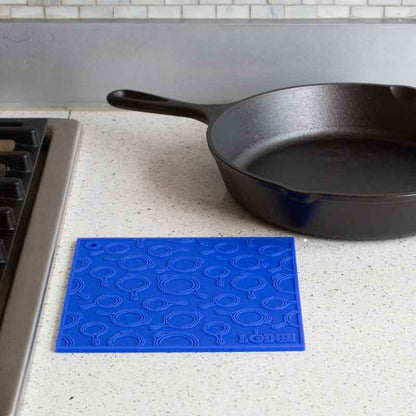 Blue silicone trivet placed flat on counter next to stove and skillet.